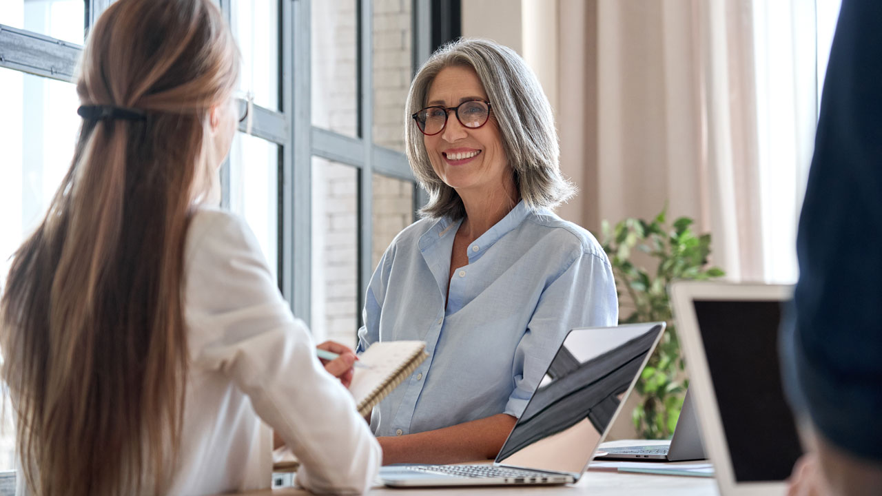 Gråhårig kvina samtalar med en person på ett kontor